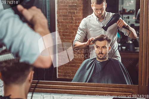 Image of Young handsome barber making haircut of attractive man in barbershop