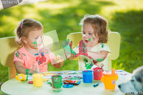 Image of Two-year old girls painting with poster paintings together against green lawn