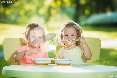 Image of Two little girls sitting at a table and eating together against green lawn