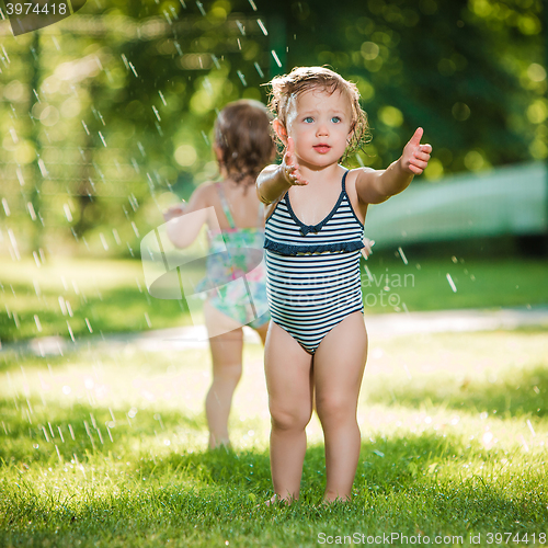 Image of The two little baby girls playing with garden sprinkler.