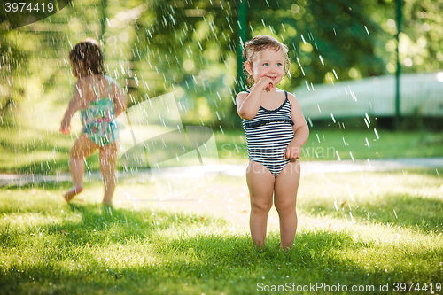 Image of The two little baby girls playing with garden sprinkler.