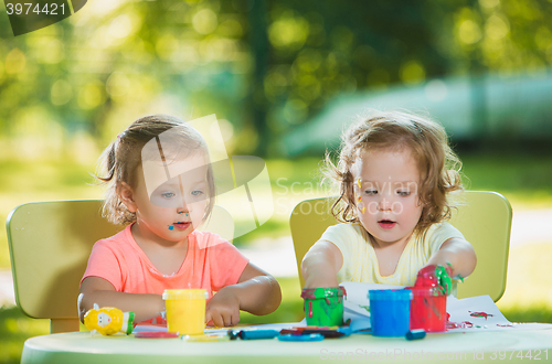 Image of Two-year old girls painting with poster paintings together against green lawn