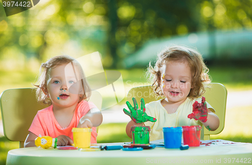 Image of Two-year old girls painting with poster paintings together against green lawn