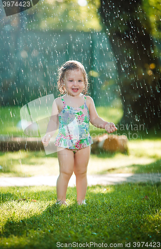 Image of The little baby girl playing with garden sprinkler.