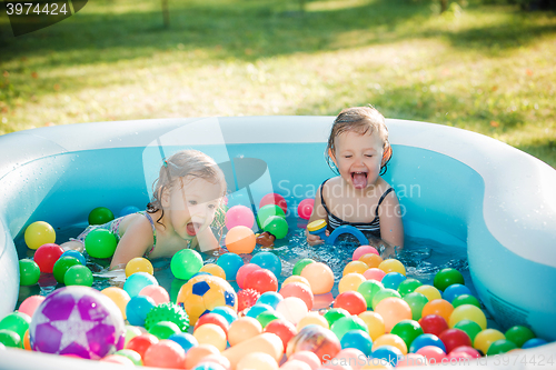 Image of The two little baby girls playing with toys in inflatable pool in the summer sunny day