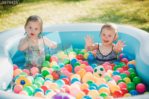 Image of The two little baby girls playing with toys in inflatable pool in the summer sunny day