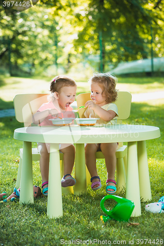 Image of Two little girls sitting at a table and eating together against green lawn