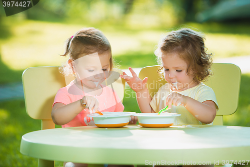 Image of Two little girls sitting at a table and eating together against green lawn