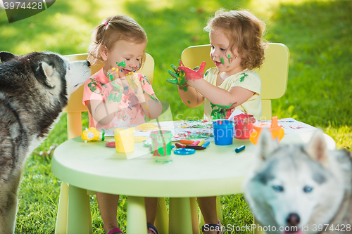 Image of Two-year old girls painting with poster paintings together against green lawn