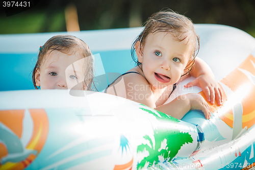 Image of The two little baby girls playing with toys in inflatable pool in the summer sunny day