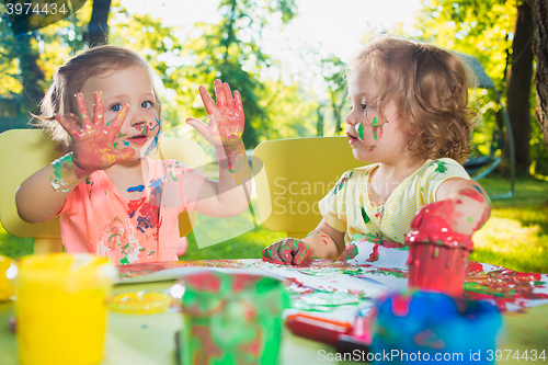 Image of Two-year old girls painting with poster paintings together against green lawn