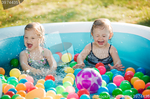 Image of The two little baby girls playing with toys in inflatable pool in the summer sunny day