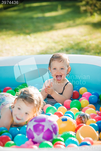 Image of The two little baby girls playing with toys in inflatable pool in the summer sunny day