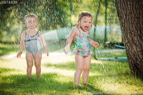 Image of The two little baby girls playing with garden sprinkler.