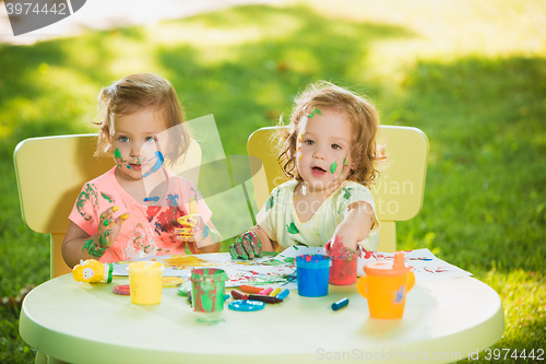 Image of Two-year old girls painting with poster paintings together against green lawn