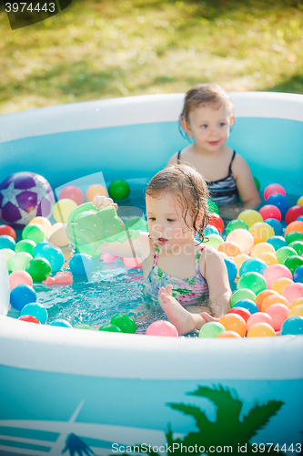 Image of The two little baby girls playing with toys in inflatable pool in the summer sunny day