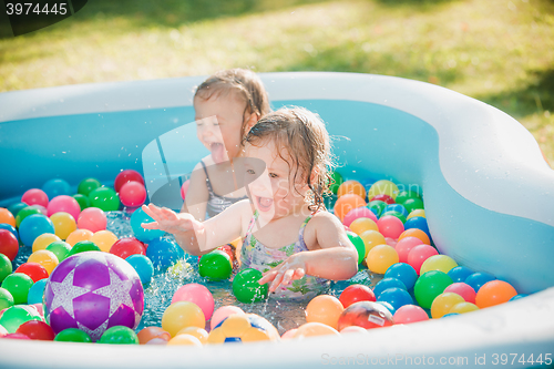 Image of The two little baby girls playing with toys in inflatable pool in the summer sunny day