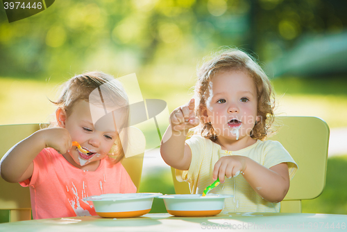 Image of Two little girls sitting at a table and eating together against green lawn