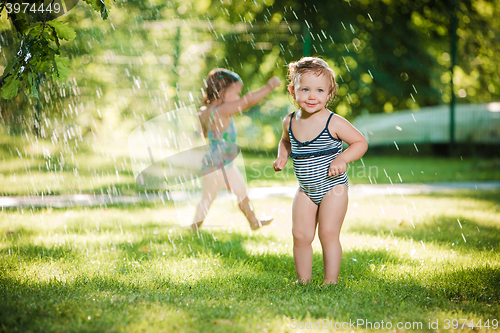 Image of The two little baby girls playing with garden sprinkler.