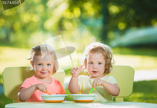 Image of Two little girls sitting at a table and eating together against green lawn