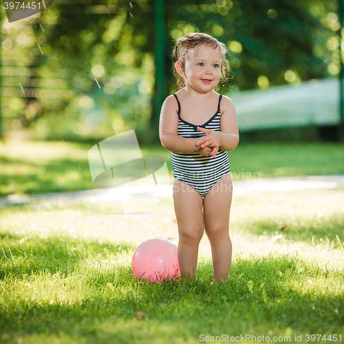 Image of The little baby girl playing with garden sprinkler.