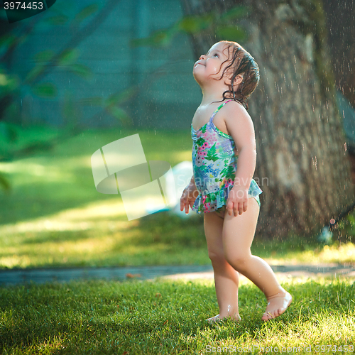 Image of The little baby girl playing with garden sprinkler.