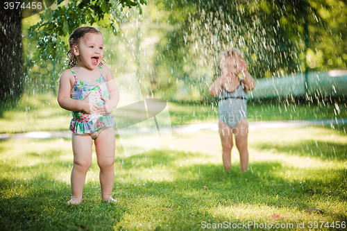 Image of The two little baby girls playing with garden sprinkler.