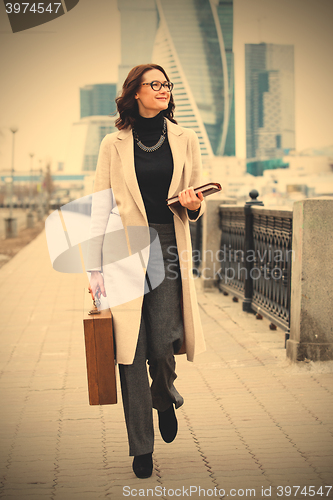 Image of beautiful smiling woman in a white coat with a wooden case and b