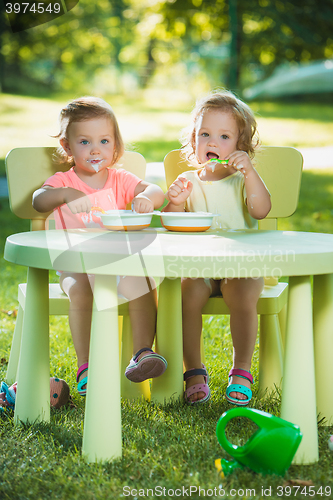 Image of Two little girls sitting at a table and eating together against green lawn