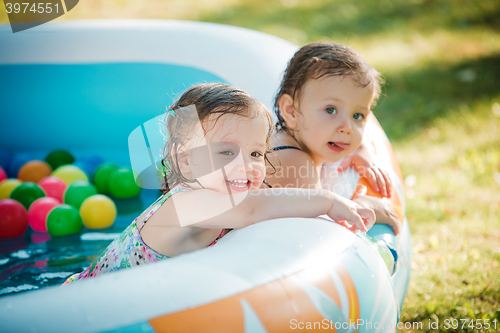 Image of The two little baby girls playing with toys in inflatable pool in the summer sunny day