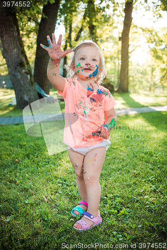 Image of Two-year old girl stained in colors against green lawn