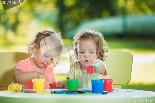 Image of Two-year old girls painting with poster paintings together against green lawn