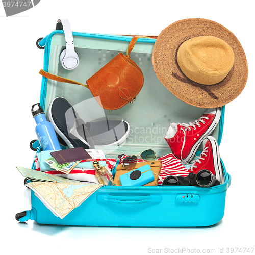 Image of The open blue suitcase, sneakers, clothing, hat, and retro camera on white background.