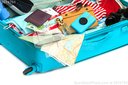 Image of The open blue suitcase, sneakers, clothing, hat, and retro camera on white background.