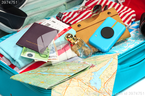 Image of The open blue suitcase, sneakers, clothing, hat, and retro camera on white background.