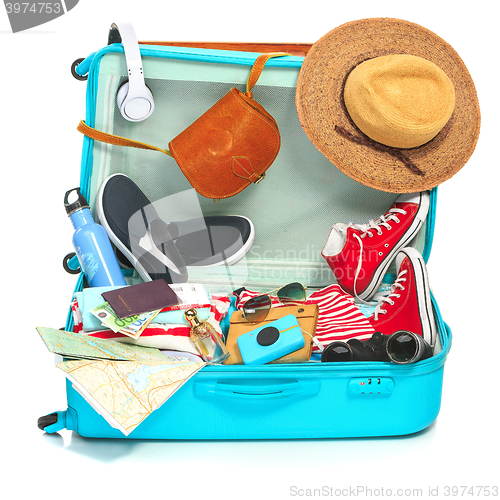 Image of The open blue suitcase, sneakers, clothing, hat, and retro camera on white background.