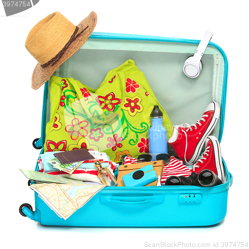 Image of The open blue suitcase, sneakers, clothing, hat, and retro camera on white background.