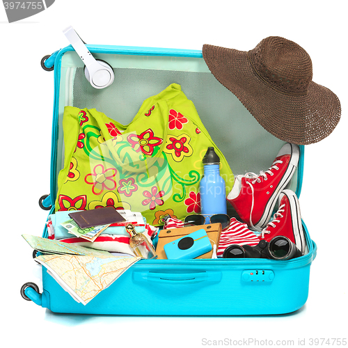 Image of The open blue suitcase, sneakers, clothing, hat, and retro camera on white background.