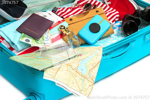 Image of The open blue suitcase, sneakers, clothing, hat, and retro camera on white background.