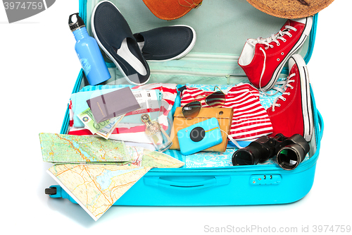 Image of The open blue suitcase, sneakers, clothing, hat, and retro camera on white background.