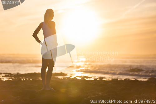 Image of Woman on sandy beach watching sunset.