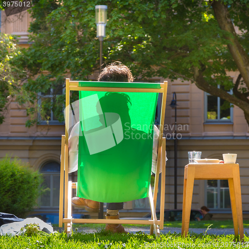 Image of Silhouette of relaxed man on deckchair in a park