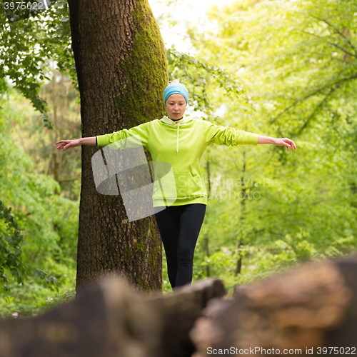 Image of Woman holding balance on tree trunk in nature.