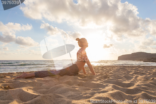 Image of Woman practicing yoga on sea beach at sunset.