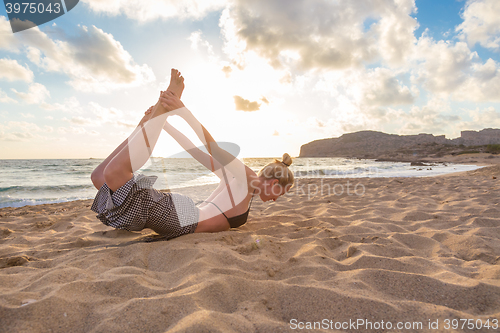 Image of Woman practicing yoga on sea beach at sunset.