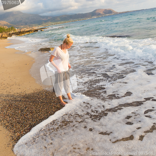 Image of Woman walking on sand beach at golden hour