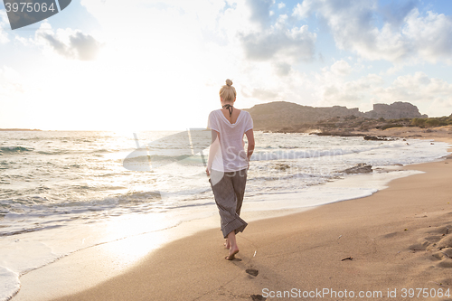 Image of Woman walking on sand beach at golden hour