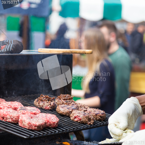 Image of Beef burgers being grilled on food stall grill.