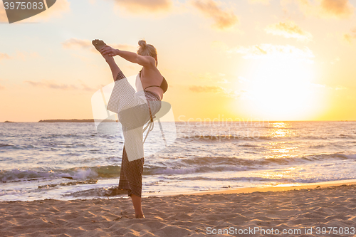 Image of Woman practicing yoga on sea beach at sunset.