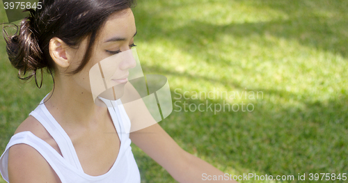 Image of Serene young woman meditating on a green lawn